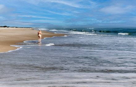 A middle aged woman stops along the shore in a clothing optional section of the beach.  Playa Linda beach located on the Cape Canaveral National seashore, Titusville, Florida